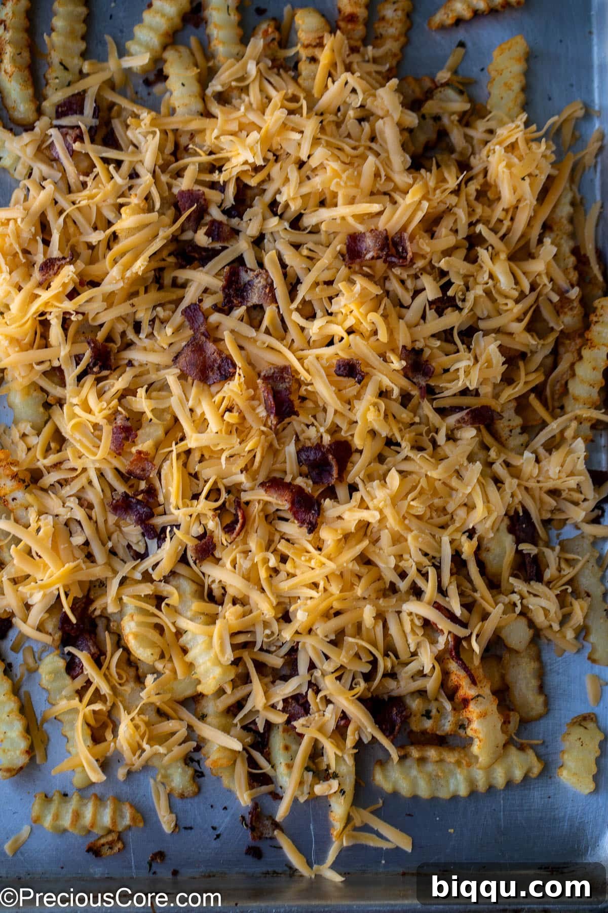 Crispy French fries topped with a generous layer of shredded cheddar cheese and crumbled bacon, ready for broiling.