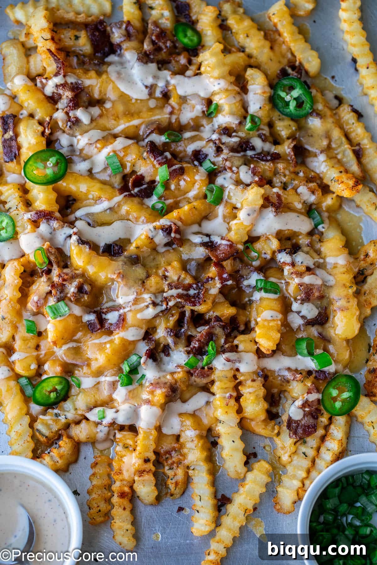 Loaded French Fries on a sheet pan, garnished with freshly sliced green onions and bright red sliced jalapeños, with ranch dressing drizzled over.