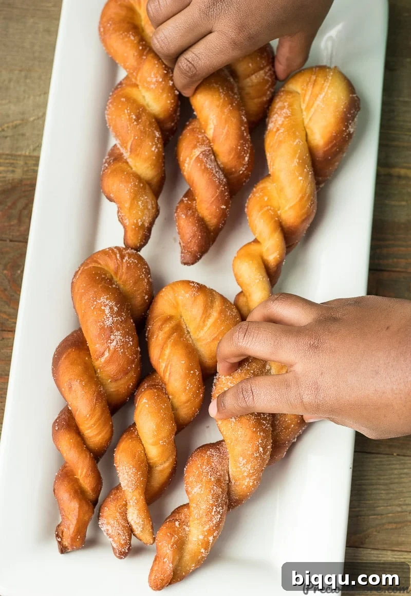 Hand grabbing a twisted African doughnut from a platter of doughnuts.