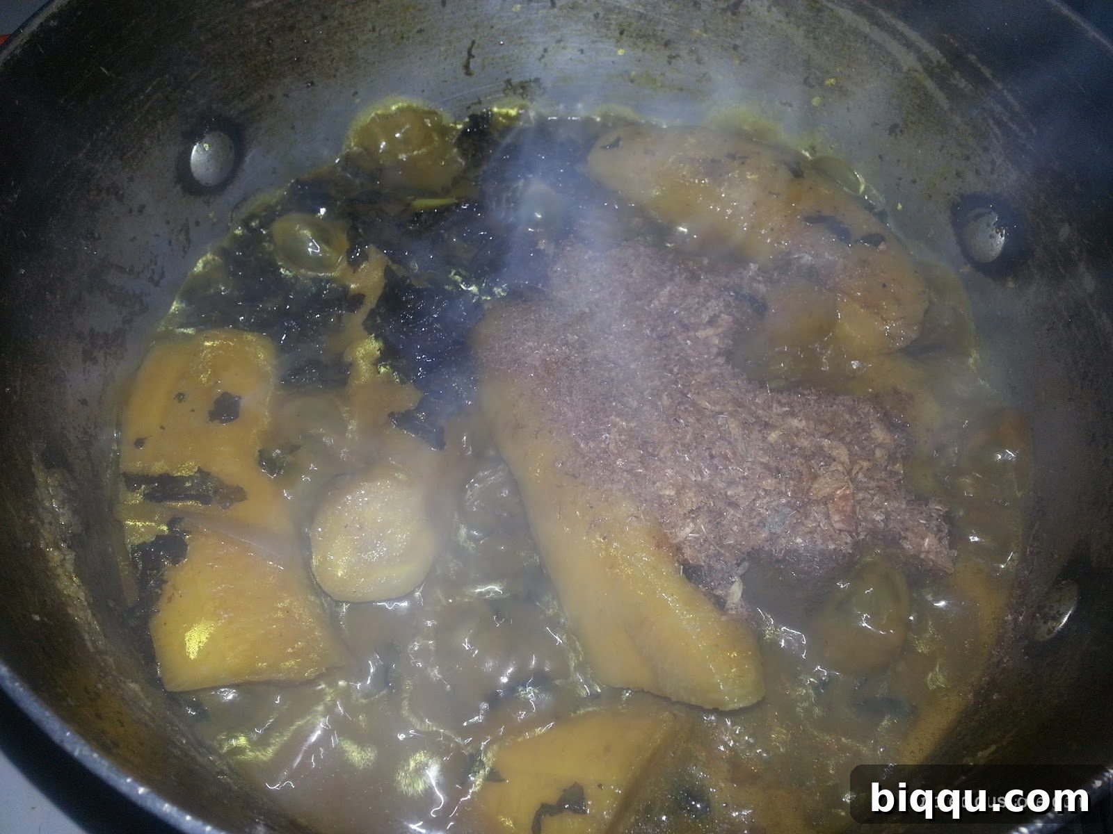 A variety of spices, including ground crayfish, seasoning cubes, and aromatics, being added to the Born House Planti pot for enhanced flavor.