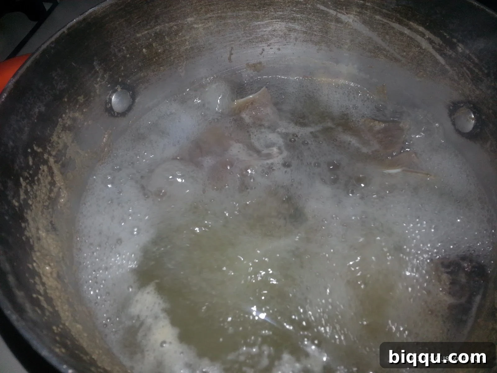 Peeled and uniformly cut unripe plantain pieces resting beside a pot of boiling smoked meat, ready for addition.
