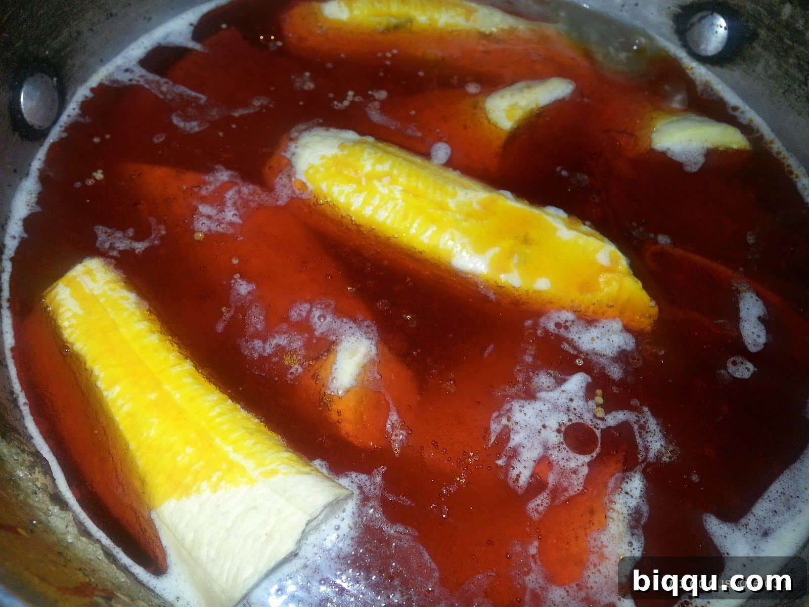 Vibrant red palm oil being poured into the pot with plantains and meat, an essential step for authentic Born House Planti.