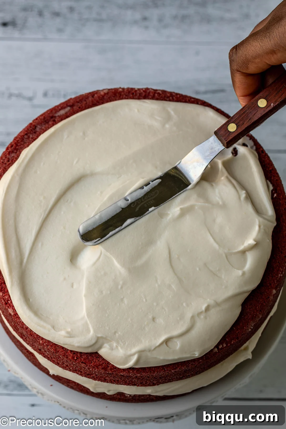 Velvet Dream Cake Without Buttermilk 14 The second layer of red velvet cake being placed and covered with cream cheese frosting, showing the cake building process.