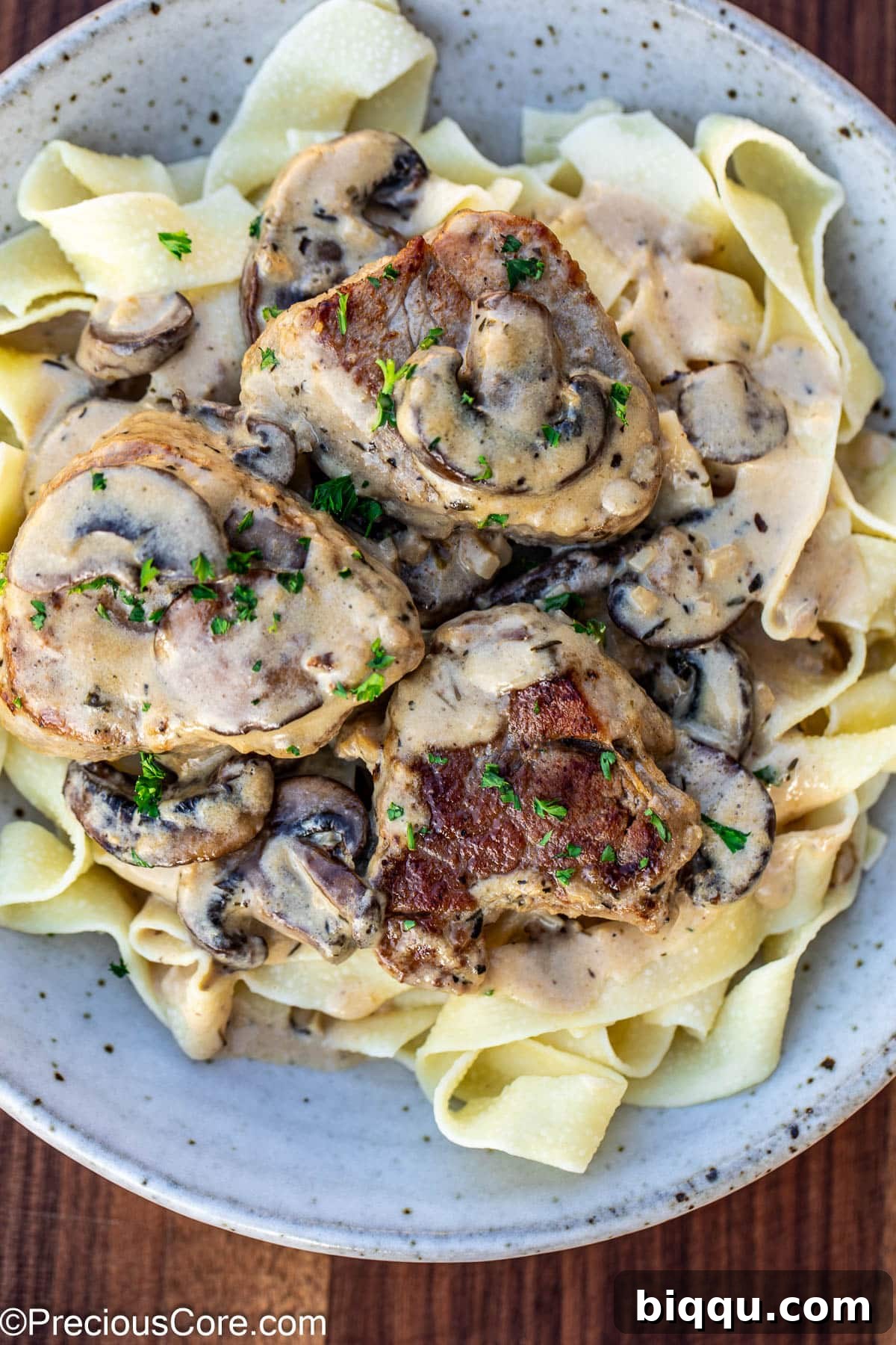 A bowl of creamy pork tenderloin and mushroom sauce, served alongside a portion of pasta, highlighting its versatility.