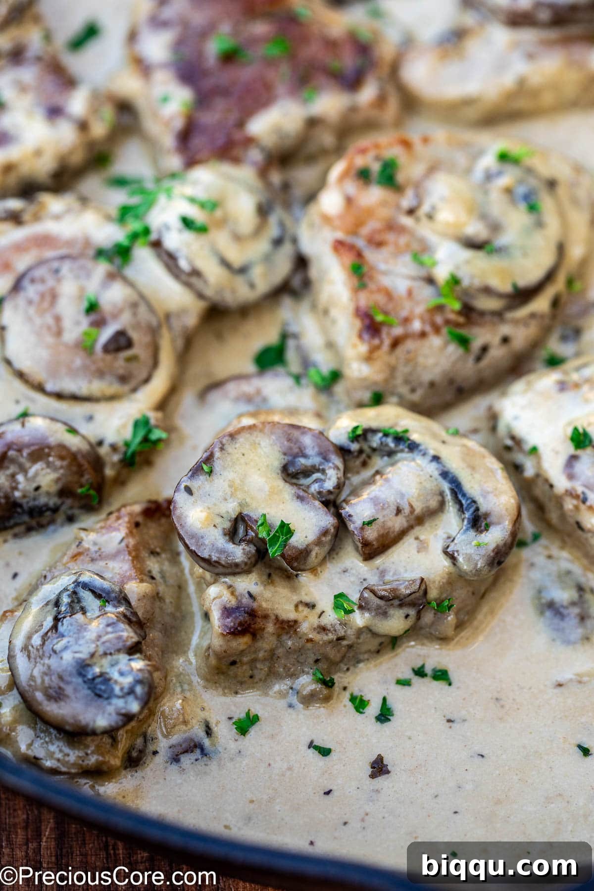 Close-up view of a pan-seared pork tenderloin medallion glistening in a thick, rich creamy mushroom sauce, showcasing its texture.