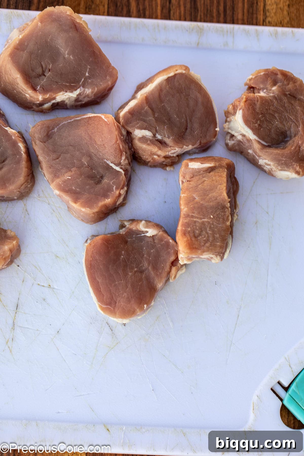 Fresh pork tenderloin being sliced into uniform medallions on a chopping board.