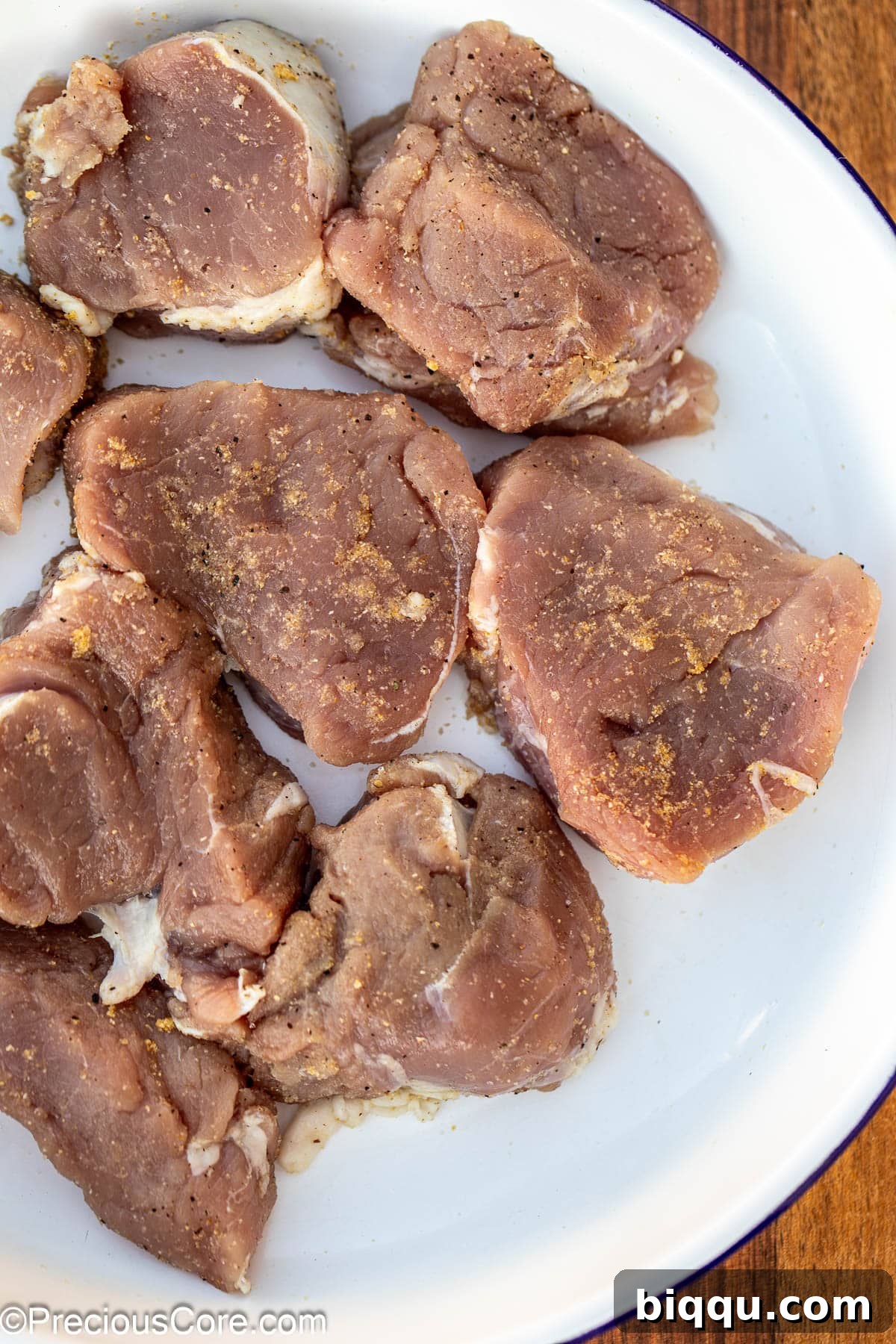 Pork tenderloin medallions seasoned with a blend of spices, resting in a white bowl, ready for searing.