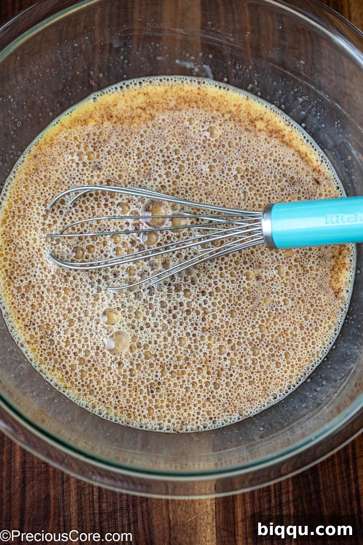 A large mixing bowl containing the whisked egg and milk mixture, with a whisk resting inside.