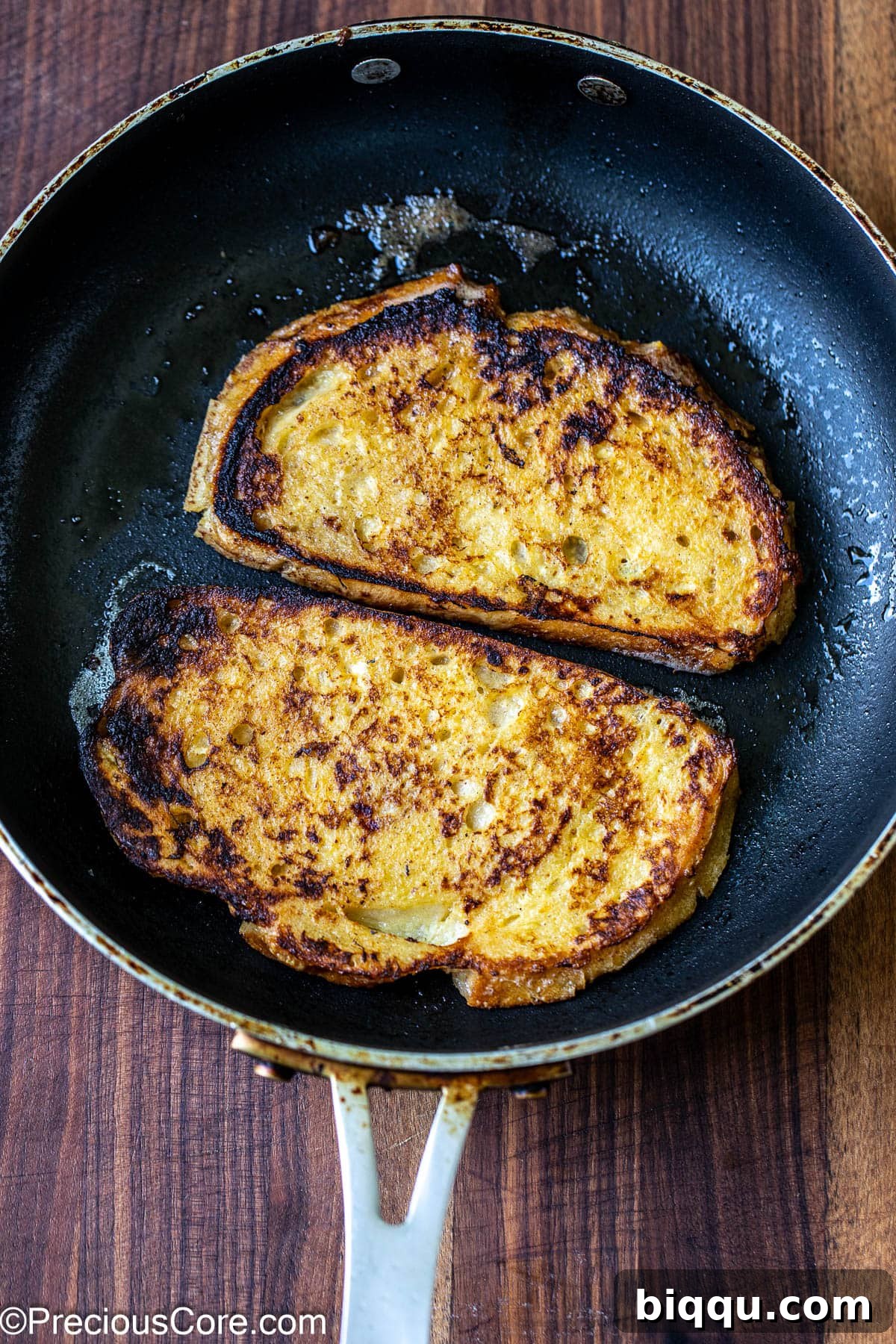 Two slices of sourdough bread cooking in a hot skillet, gently browning on the stovetop.