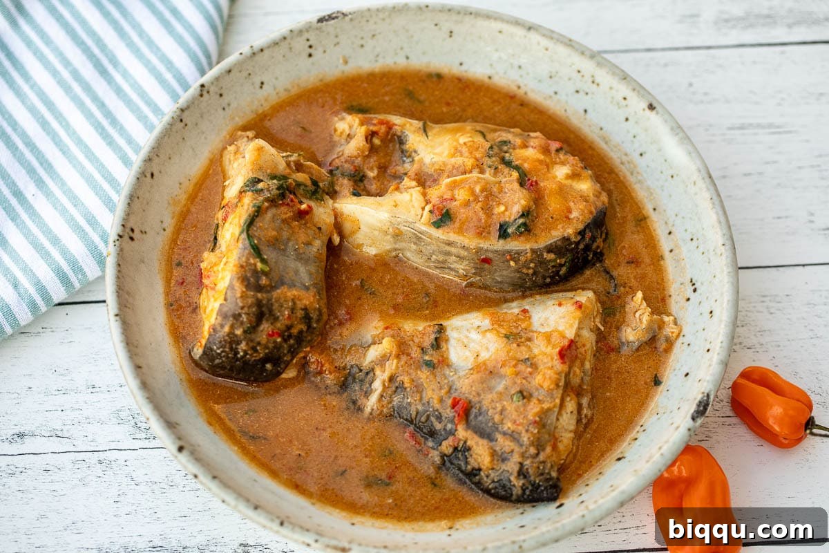 A wide, inviting shot of Nigerian pepper soup served in a traditional setting, showcasing its vibrant color and tempting steam.