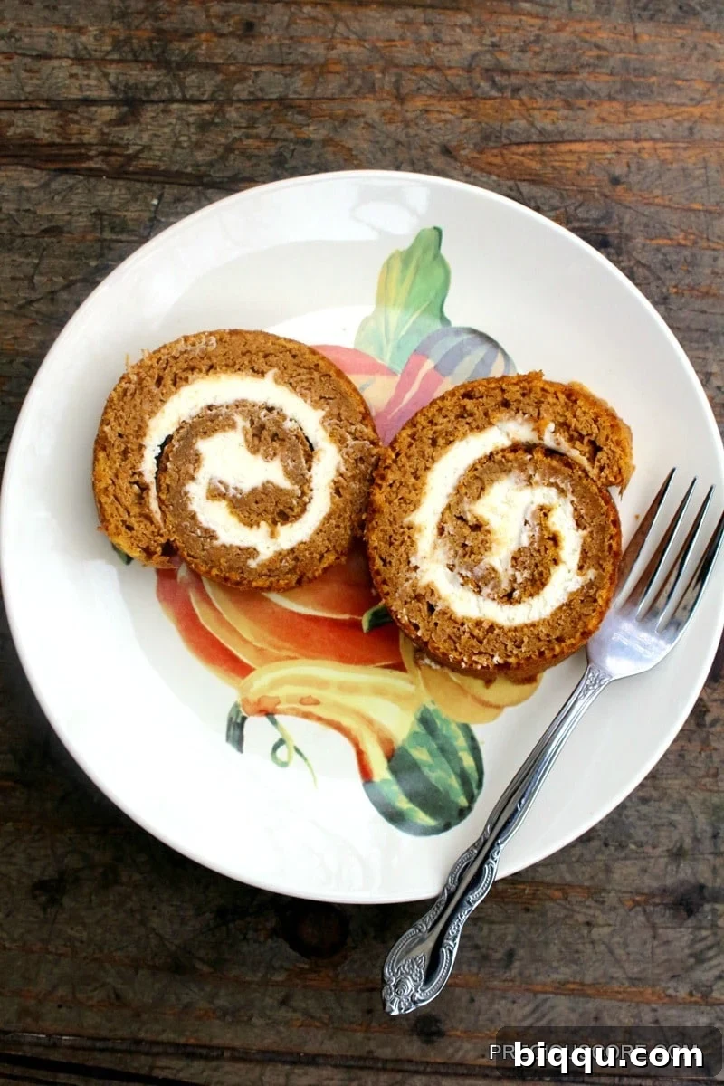 Two slices of pumpkin roll cake on a plate with a fork, ready to be enjoyed.