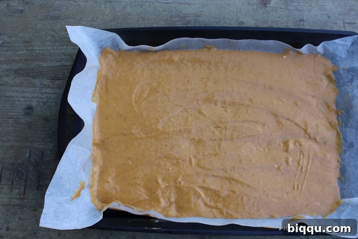 Pumpkin roll cake batter spread evenly in a parchment-lined baking pan.