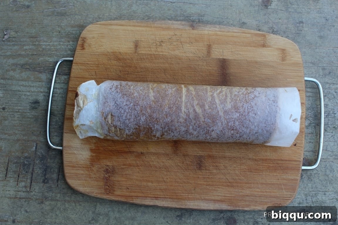Pumpkin cake freshly rolled with parchment paper on a wooden cutting board.