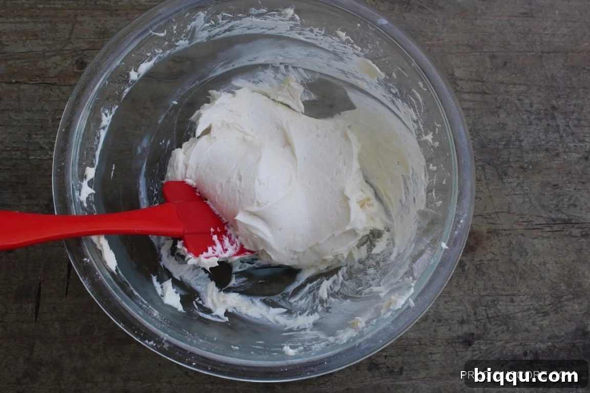 A red spatula mixing cream cheese filling ingredients to a smooth consistency.