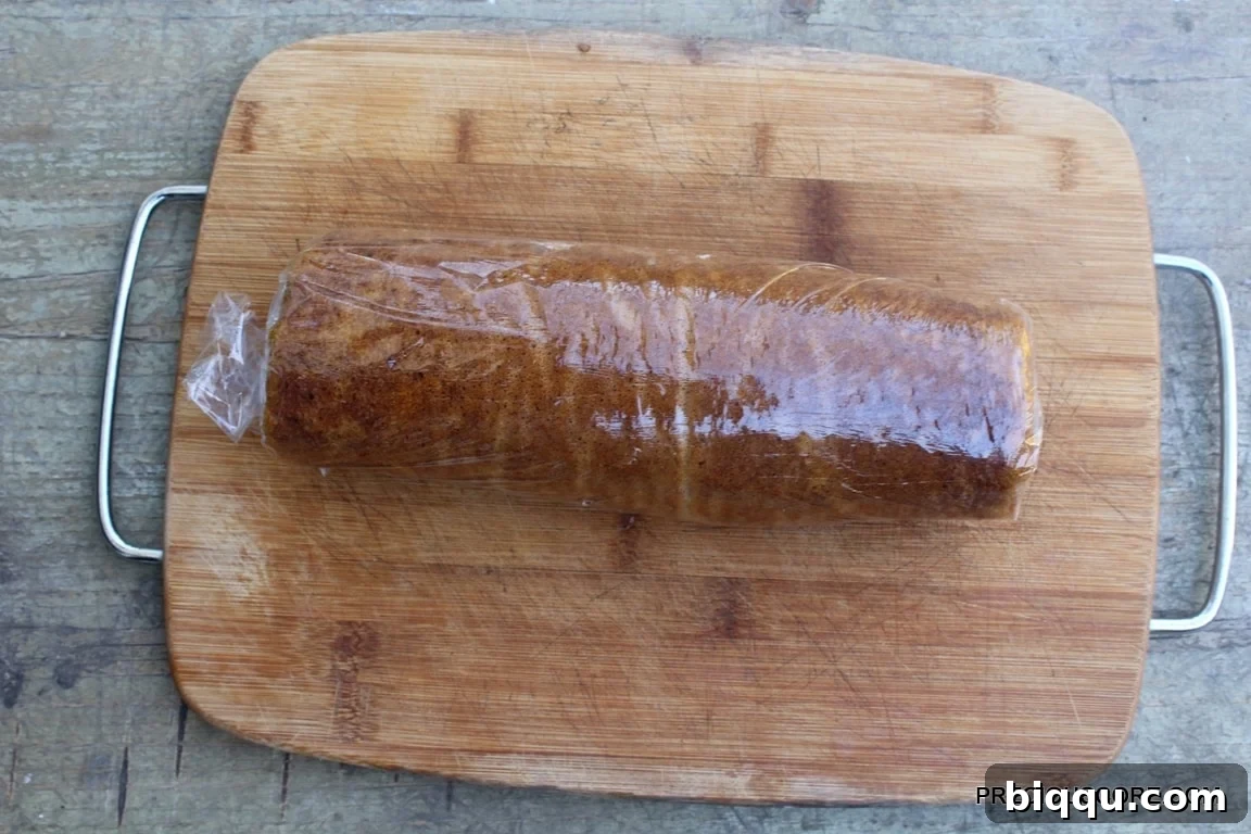 Pumpkin cake with cream cheese filling, expertly rolled together on a wooden cutting board.