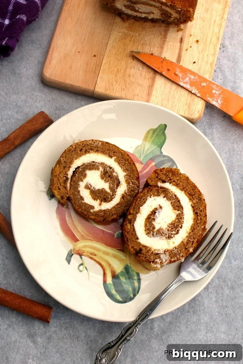 Two perfect slices of pumpkin roll cake artfully arranged on a decorated plate with a fork.
