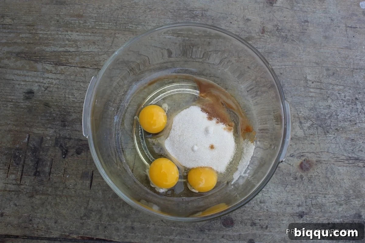 Eggs, sugar, and vanilla extract ready for mixing in a glass bowl.