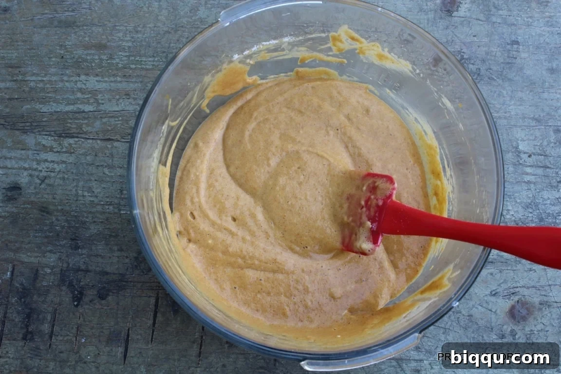 A bowl of smooth, orange pumpkin roll cake batter, ready for baking.