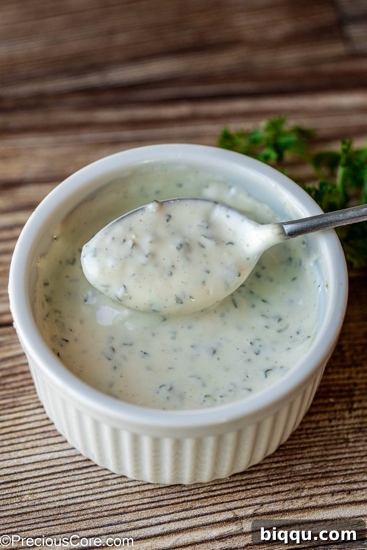 A small ramekin filled with freshly made, creamy white shawarma sauce, garnished with finely chopped fresh herbs.