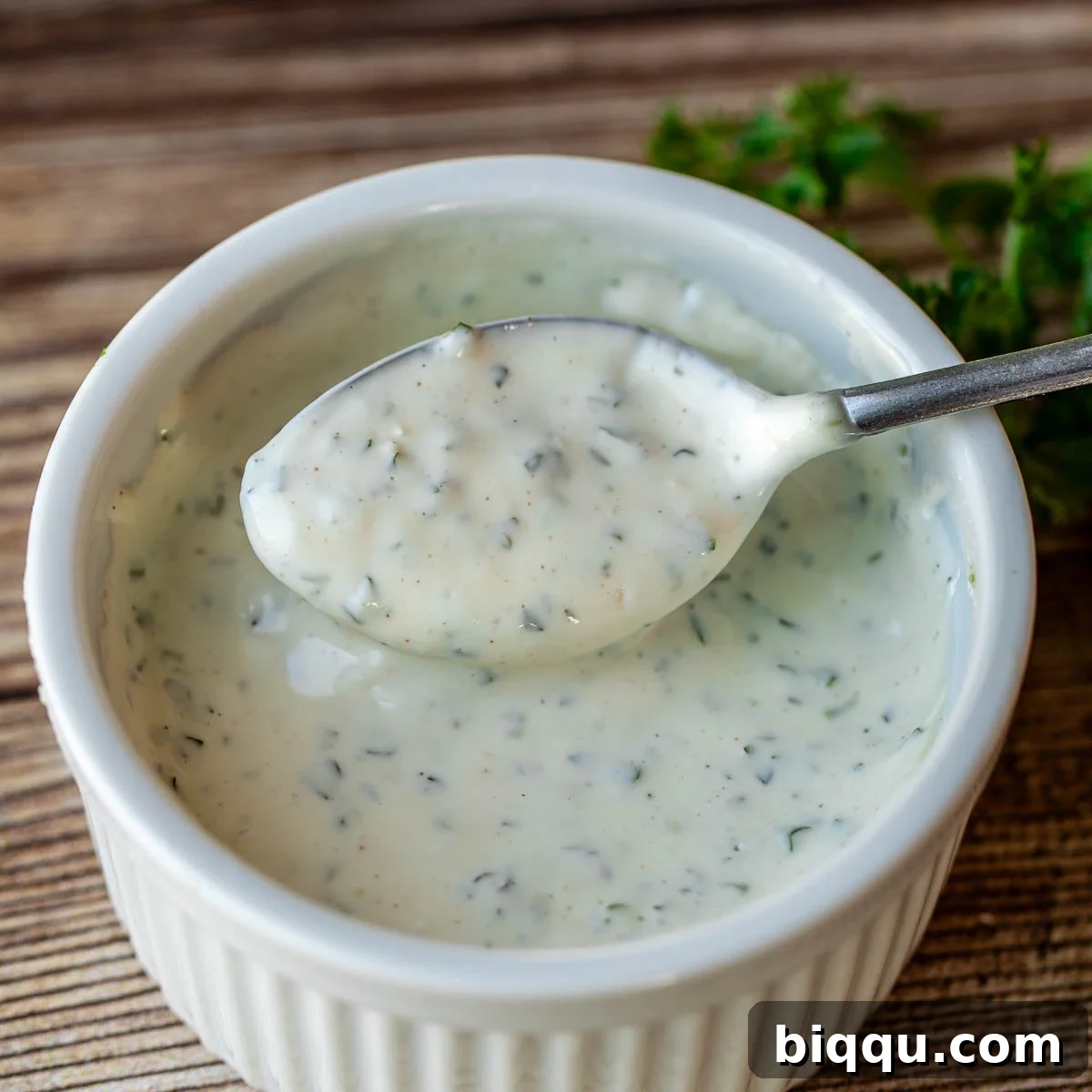A spoon lifting a creamy dollop of homemade shawarma sauce from a bowl, highlighting its smooth and thick consistency.