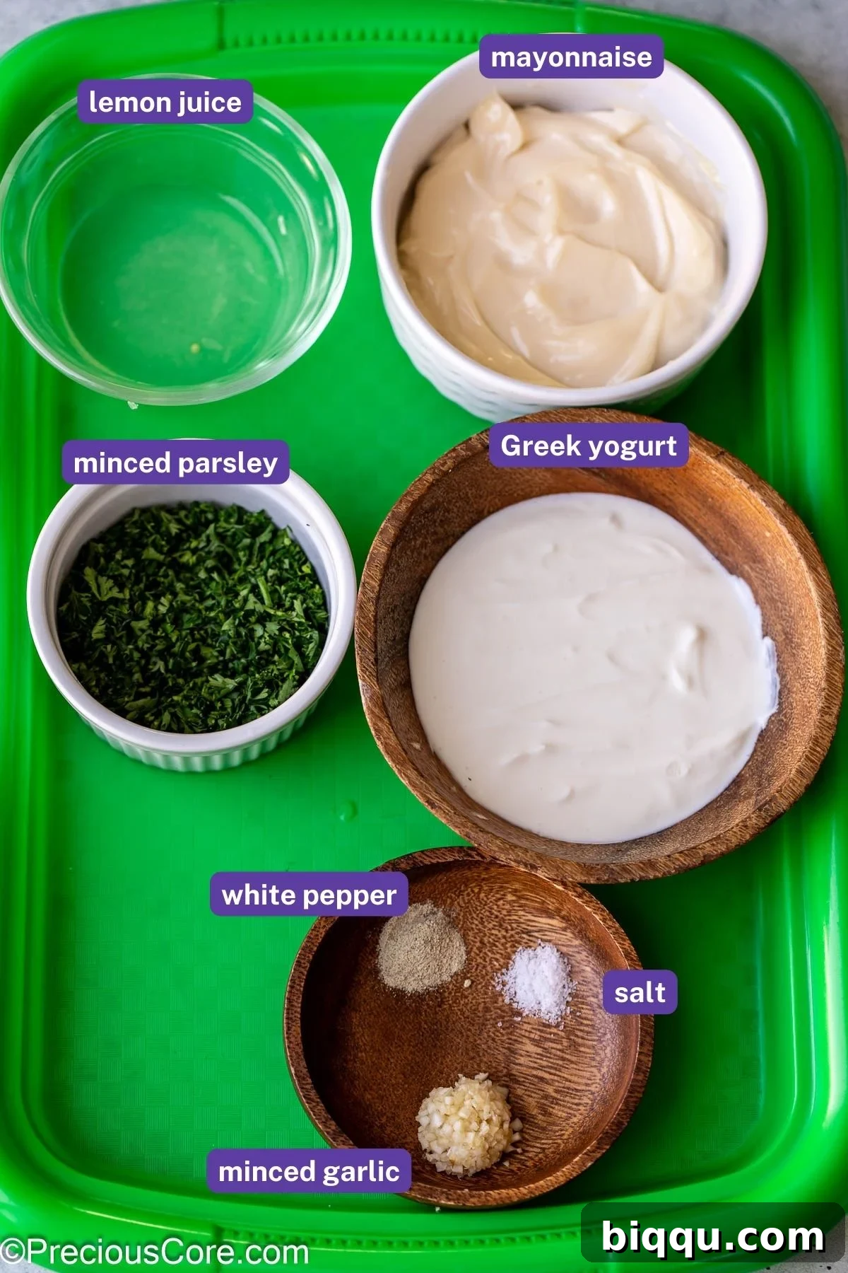 Close-up of fresh ingredients laid out for making shawarma sauce, including a bowl of Greek yogurt, a jar of mayonnaise, whole garlic cloves, and fresh parsley.