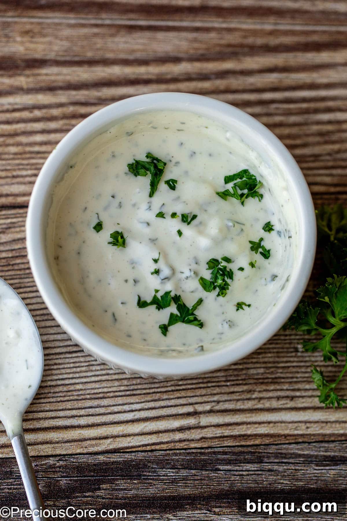 A beautifully presented bowl of creamy white garlic shawarma sauce, garnished with a sprinkle of fresh green herbs.