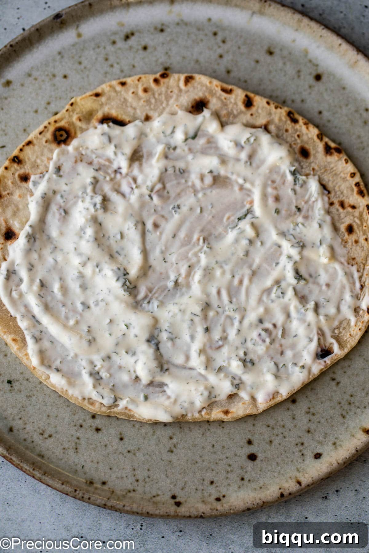 Creamy white shawarma sauce drizzled generously over a piece of warm, fluffy flatbread, showcasing its inviting texture.