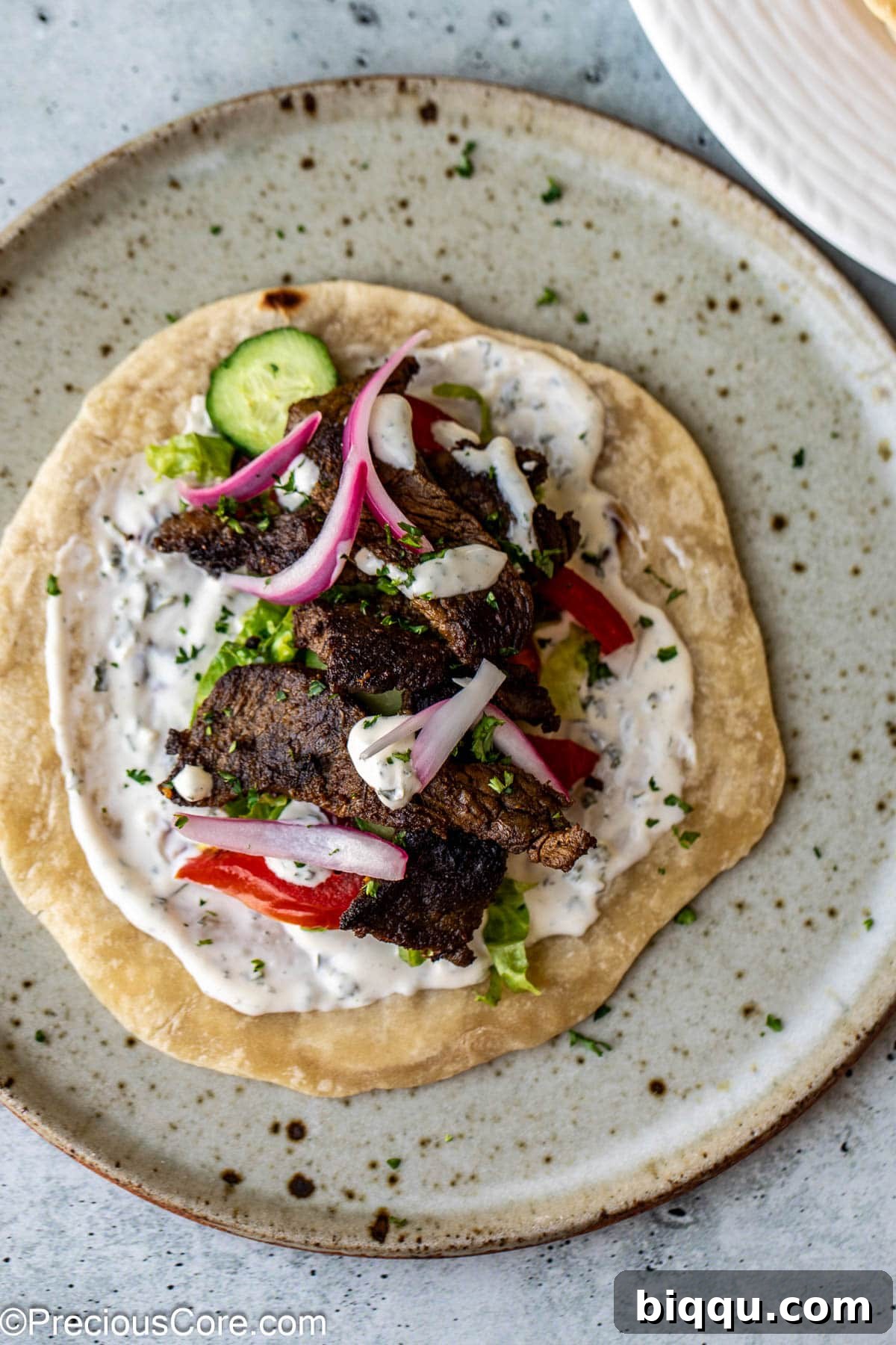 A flatbread topped with beef shawarma, veggies, and sauce.
