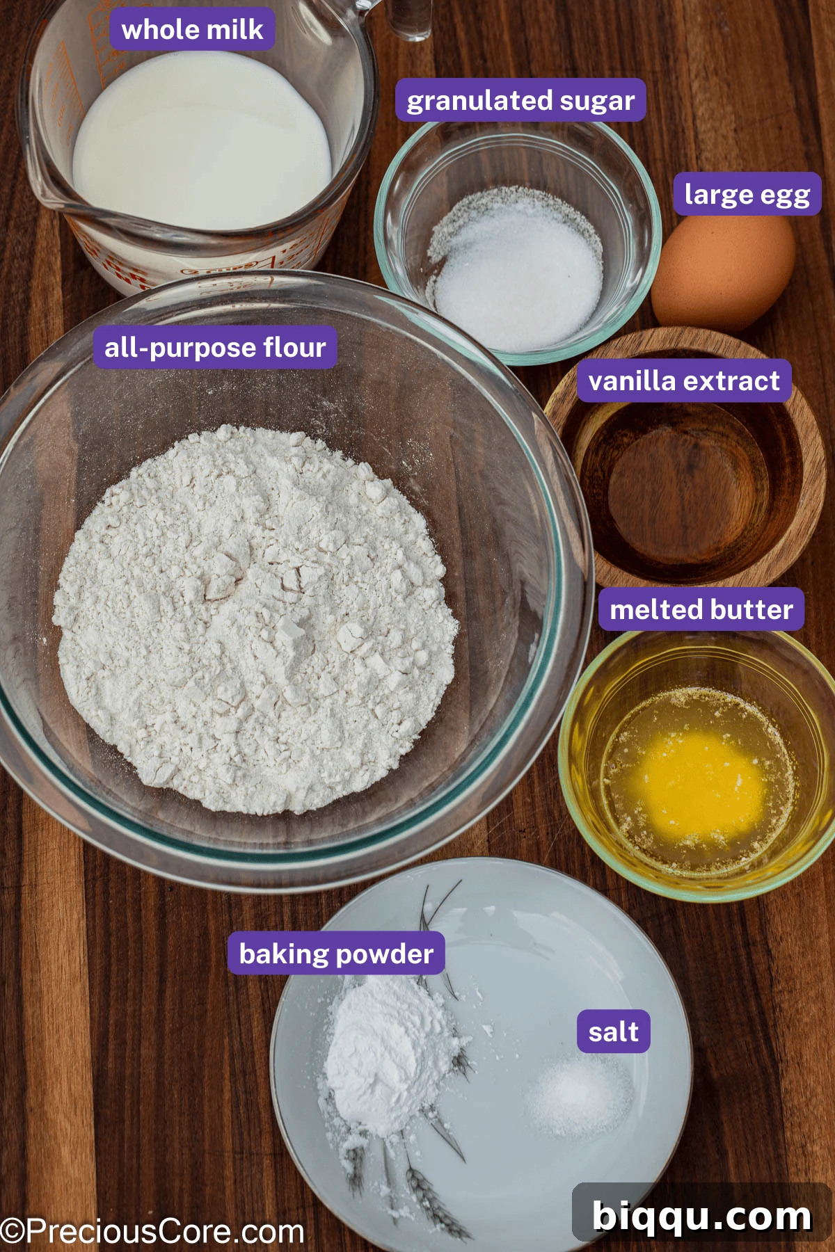 Pancake ingredients, including flour, milk, eggs, and butter, neatly labeled on a wooden surface.