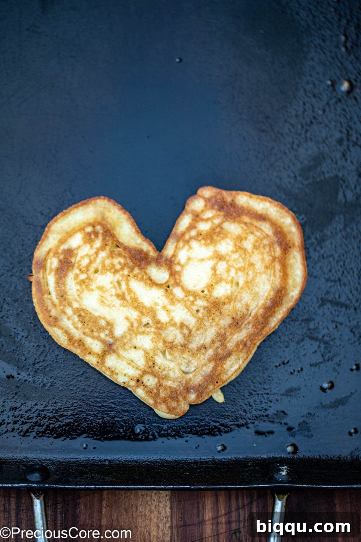 A perfectly cooked golden-brown heart-shaped pancake on a griddle.