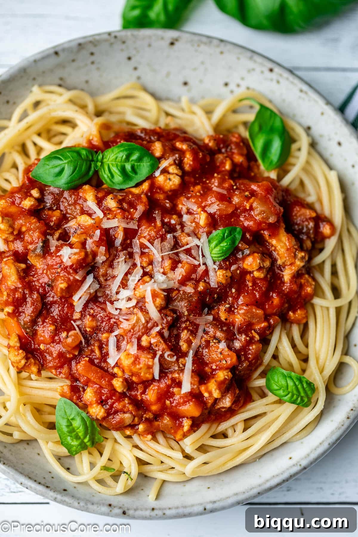 A generous serving of spaghetti in a white bowl, generously topped with a rich chicken Bolognese sauce and a sprinkle of fresh herbs.