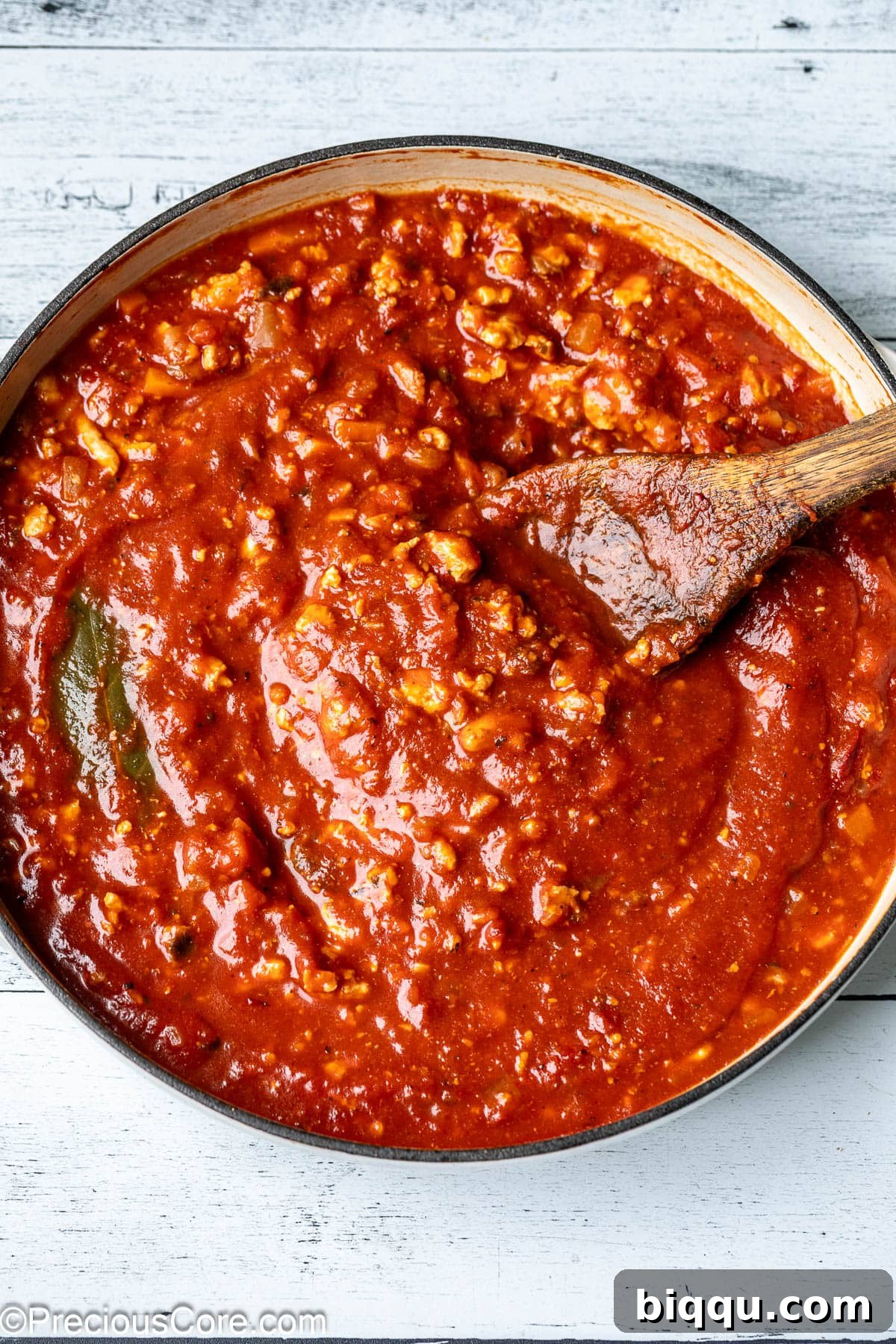 A pot of vibrant red chicken Bolognese sauce, rich and thick, simmering gently on the stovetop, indicating it's nearly ready to serve.