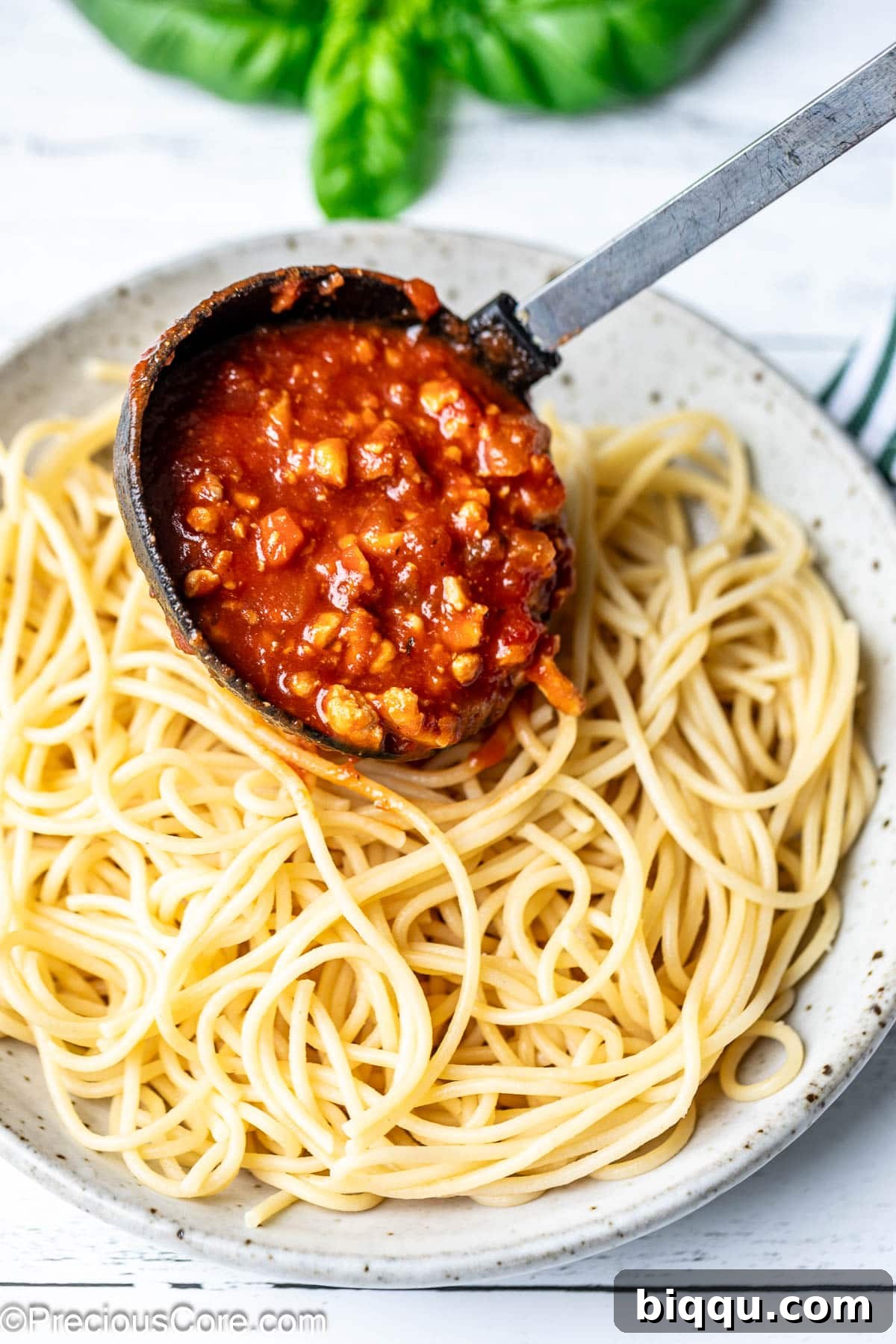 A thick, savory red Bolognese sauce with ground chicken is being poured from a pot over a generous serving of cooked spaghetti in a bowl.
