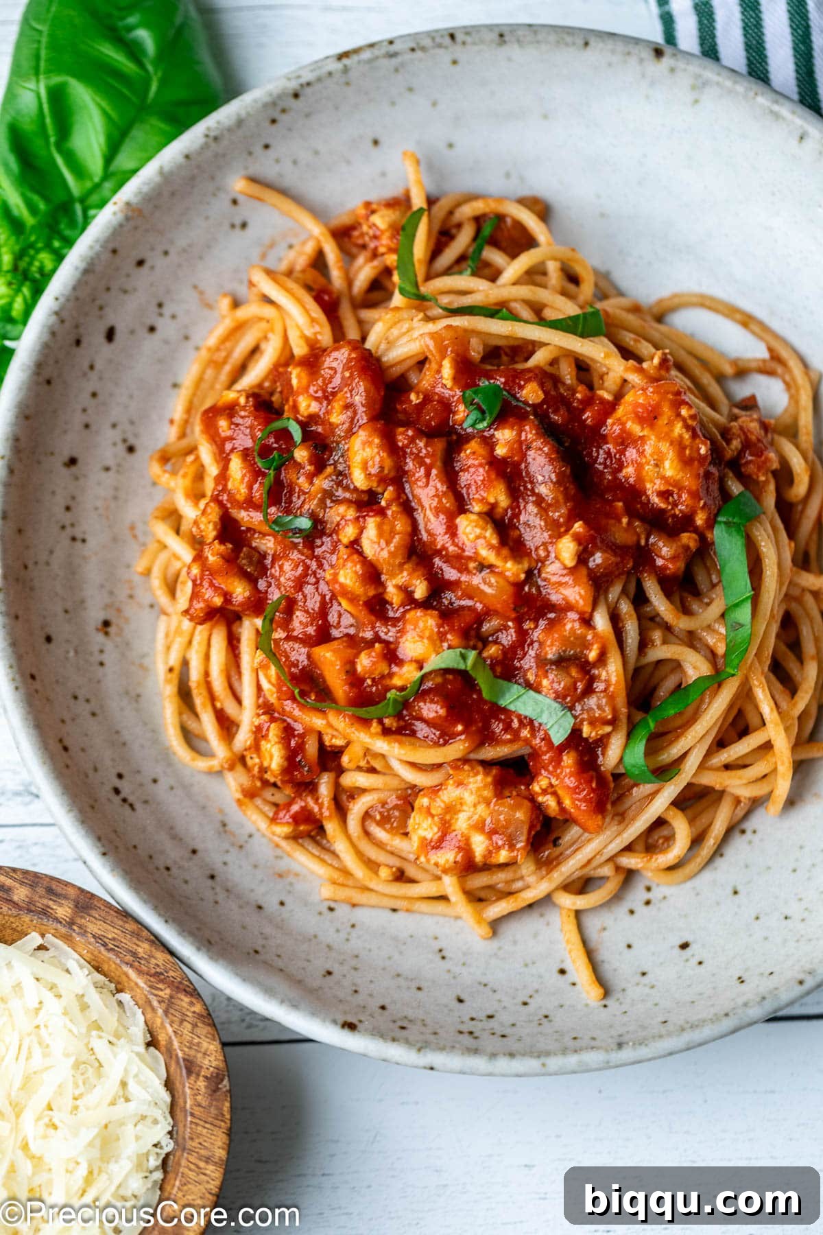 A close-up of spaghetti tossed evenly with a rich red chicken Bolognese sauce in a large bowl, ready to be served.