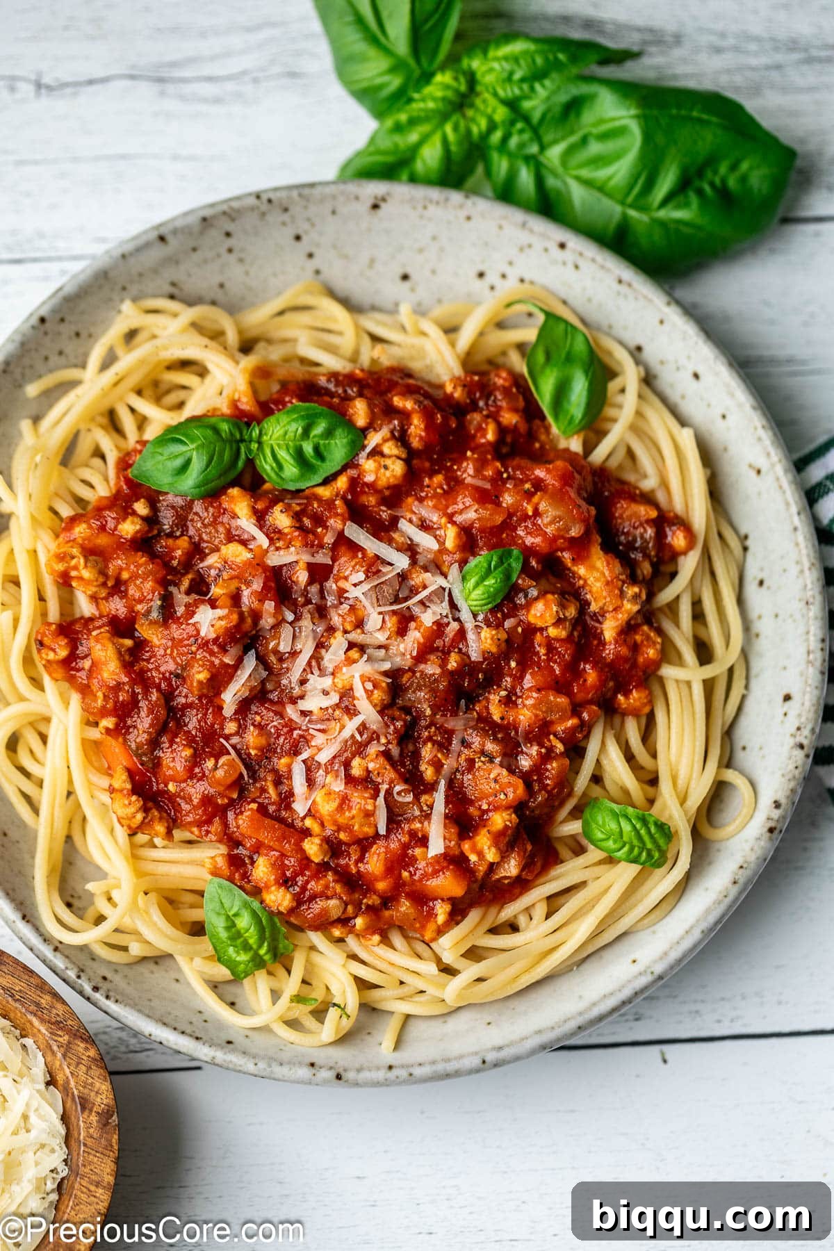 A beautifully plated bowl of chicken spaghetti Bolognese, garnished with fresh basil leaves and a generous dusting of Parmesan cheese.