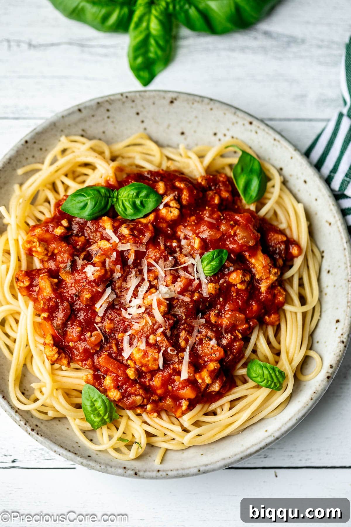 A bowl of chicken spaghetti Bolognese, generously topped with shredded Parmesan cheese and fresh basil, ready to be enjoyed.