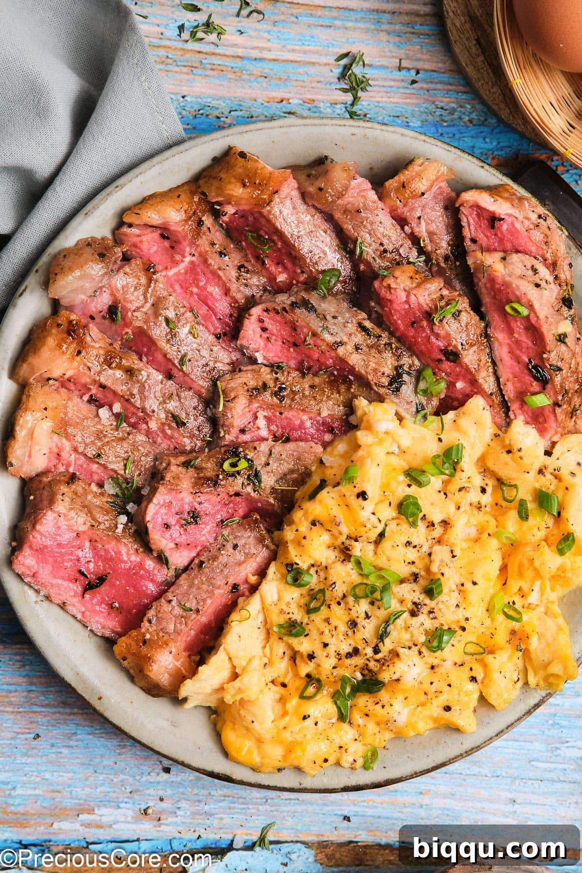 Close-up of a succulent seared steak with soft, creamy scrambled eggs on a white plate, garnished with fresh herbs.