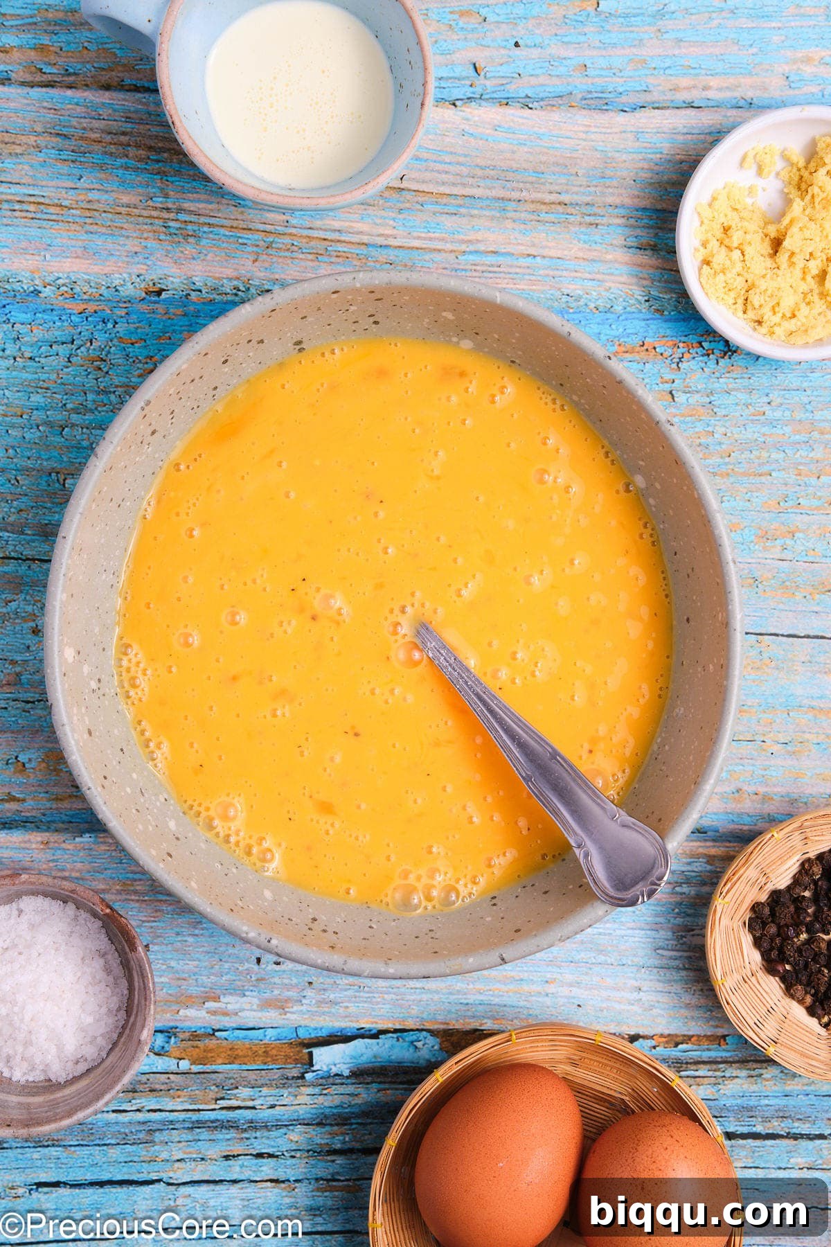 A whisked scrambled egg mixture, smooth and pale yellow, in a glass bowl.