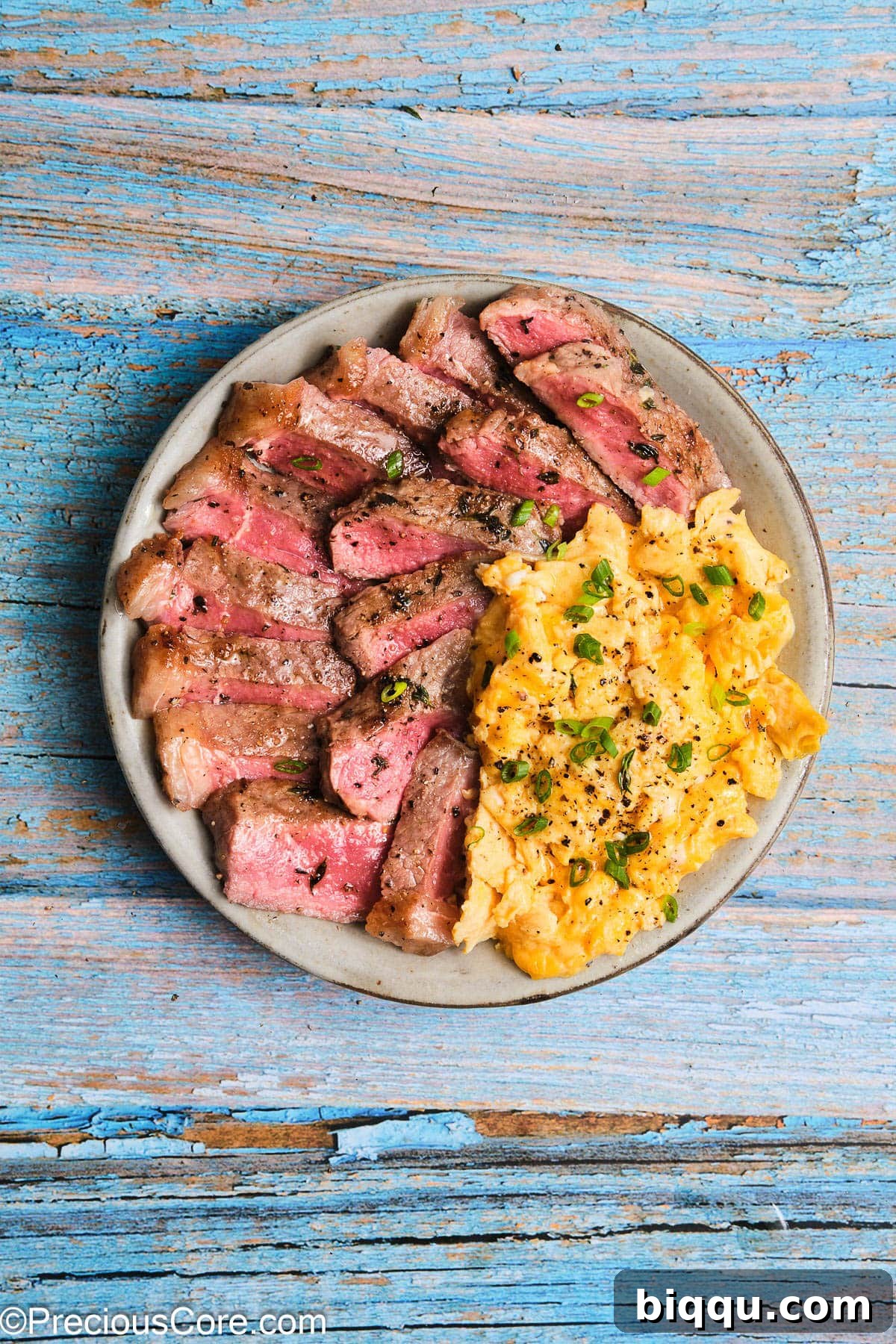 A beautifully arranged plate featuring tender slices of steak next to a generous portion of soft scrambled eggs.