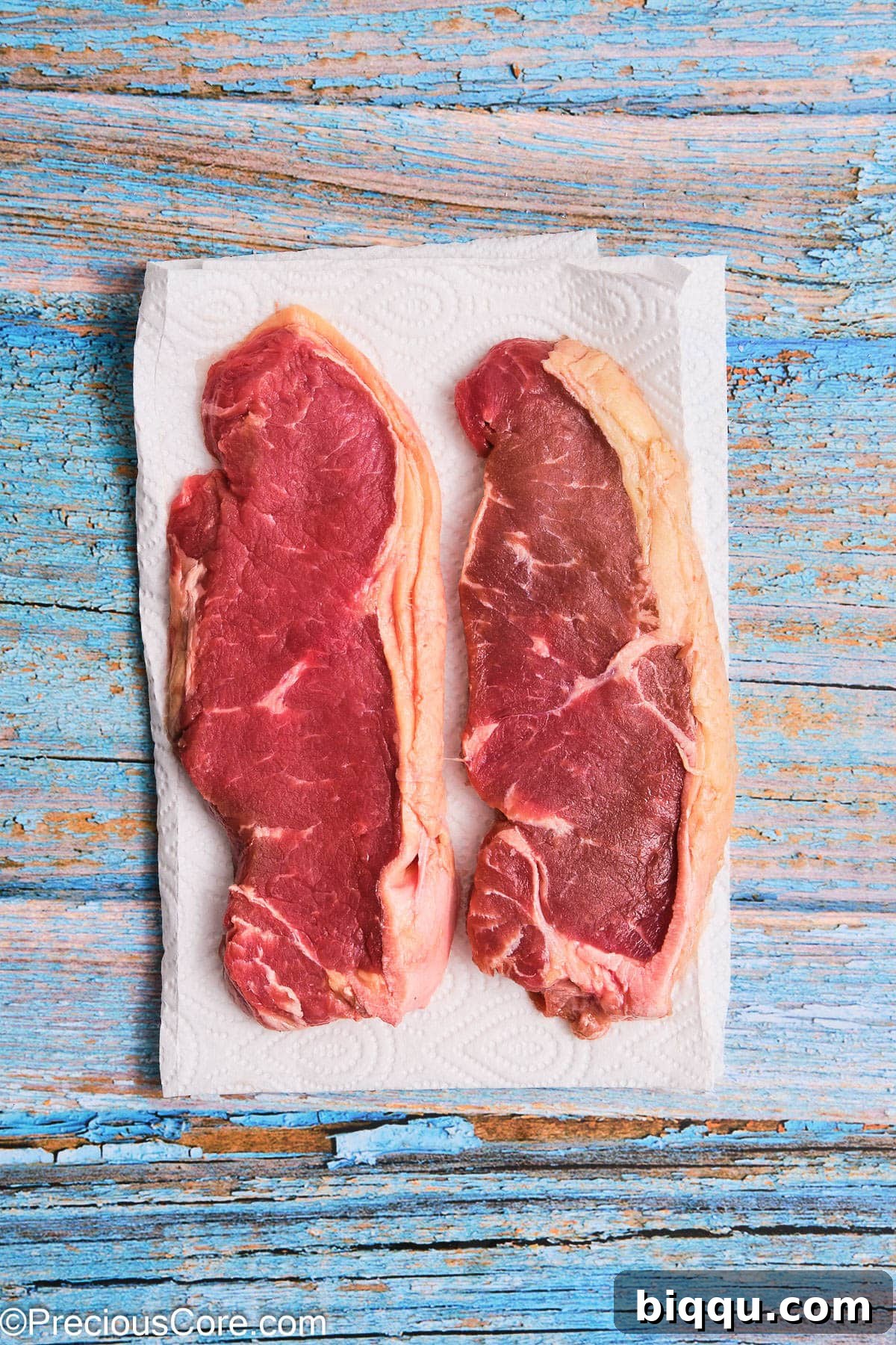 Two raw ribeye steaks resting on paper towels, ready for preparation.