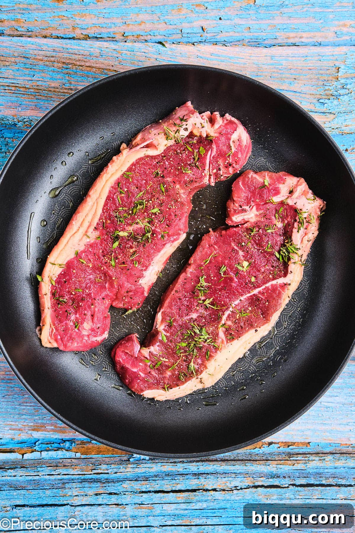 Seasoned steaks sizzling in a hot non-stick skillet, beginning to form a crust.