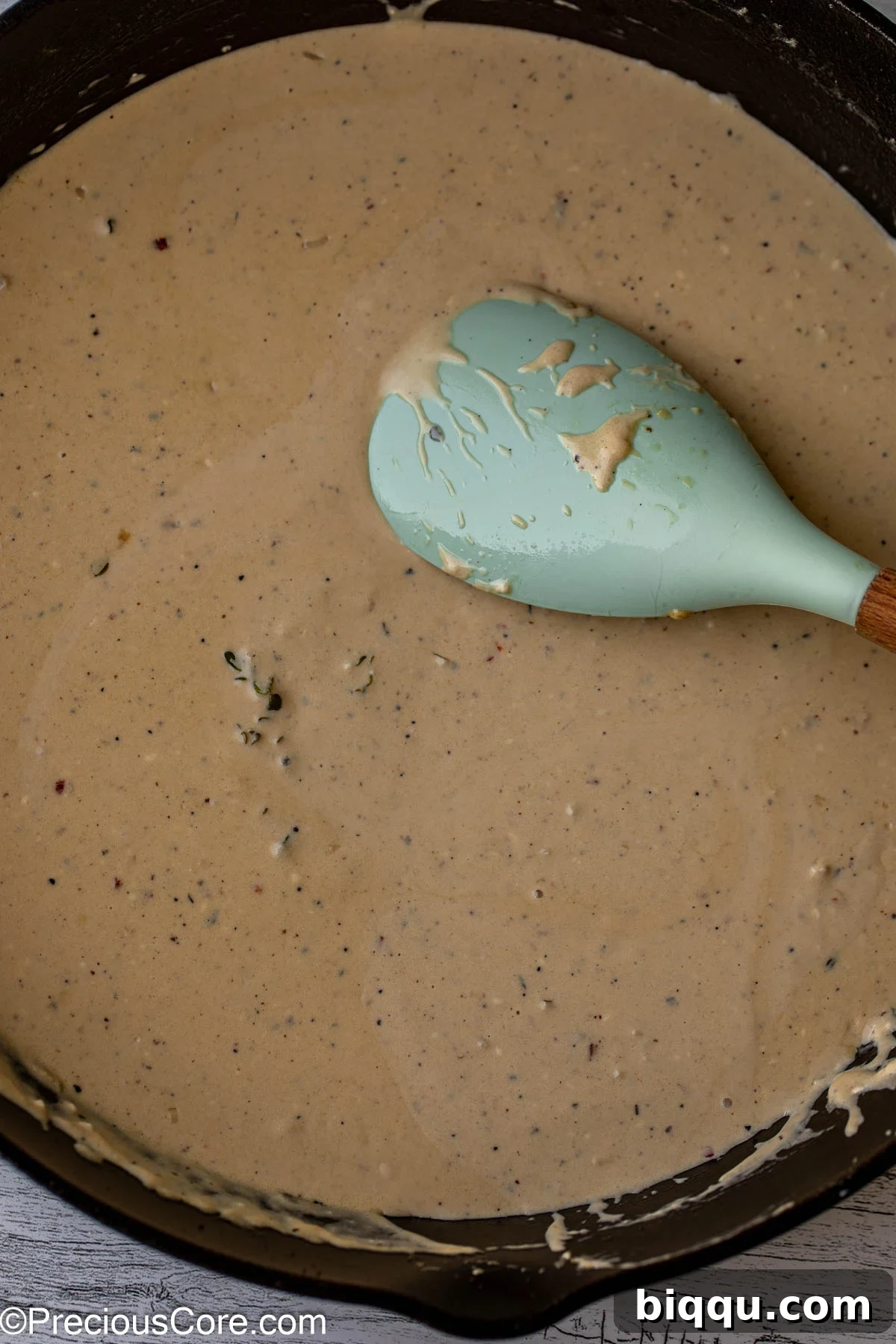 Stirring homemade cream sauce with a large spoon in a skillet.