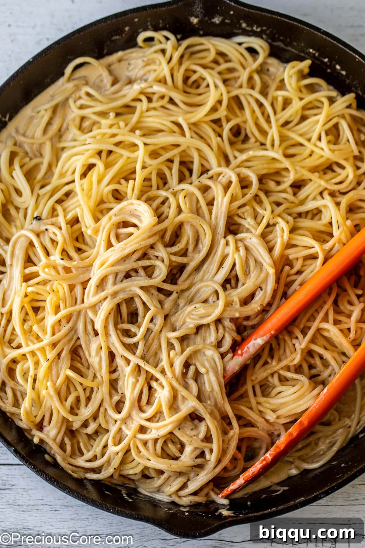Cooked spaghetti pasta being tossed in garlic cream sauce.