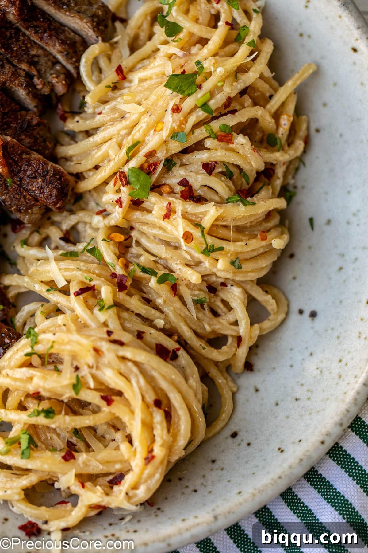 Steak and Pasta dinner served with red pepper flakes and a glass of wine.