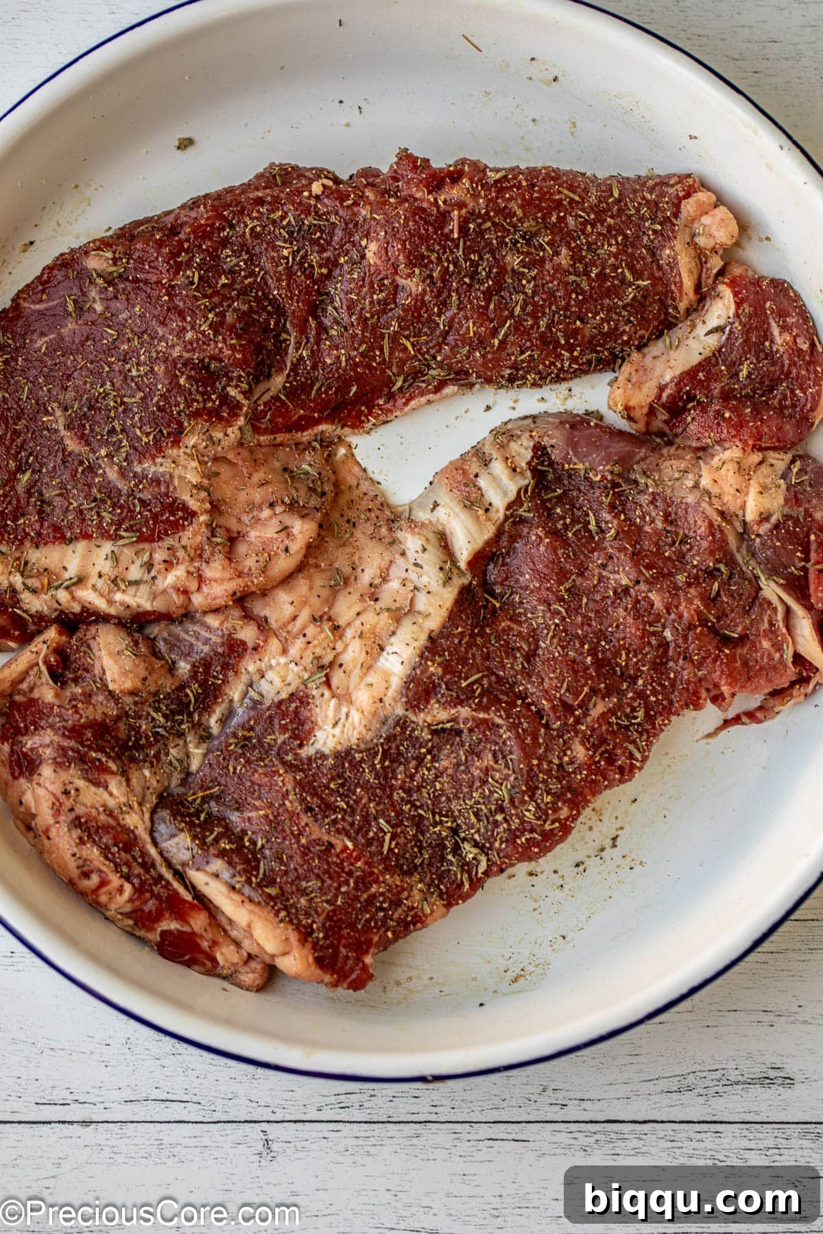 Raw ribeye steaks seasoned with herbs and spices.