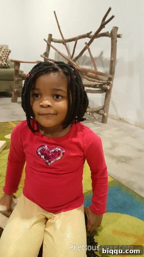 A young girl with yarn braids, smiling brightly.