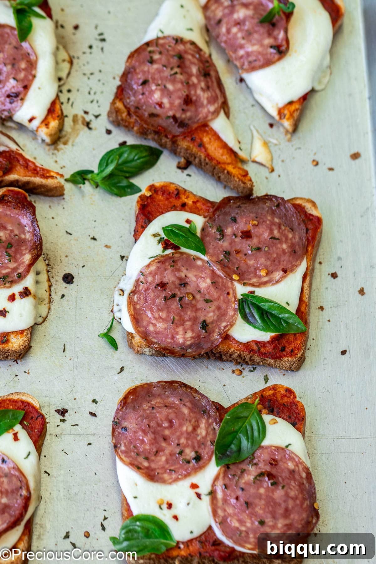 Close-up view of freshly baked pizza toasts on a baking sheet, showcasing melted cheese and toppings.