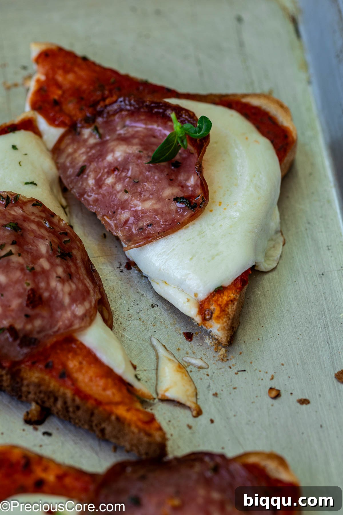 A perfectly cut triangular slice of pizza toast, showing off melted cheese and toppings.