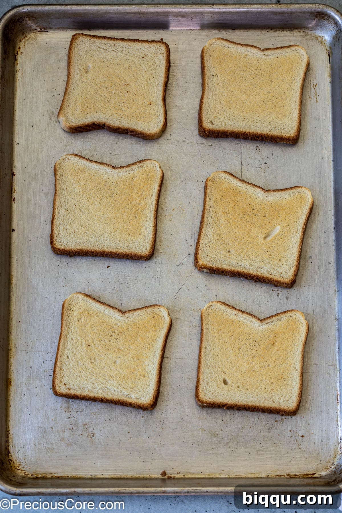 Lightly toasted bread slices laid out on a baking sheet, ready for toppings.