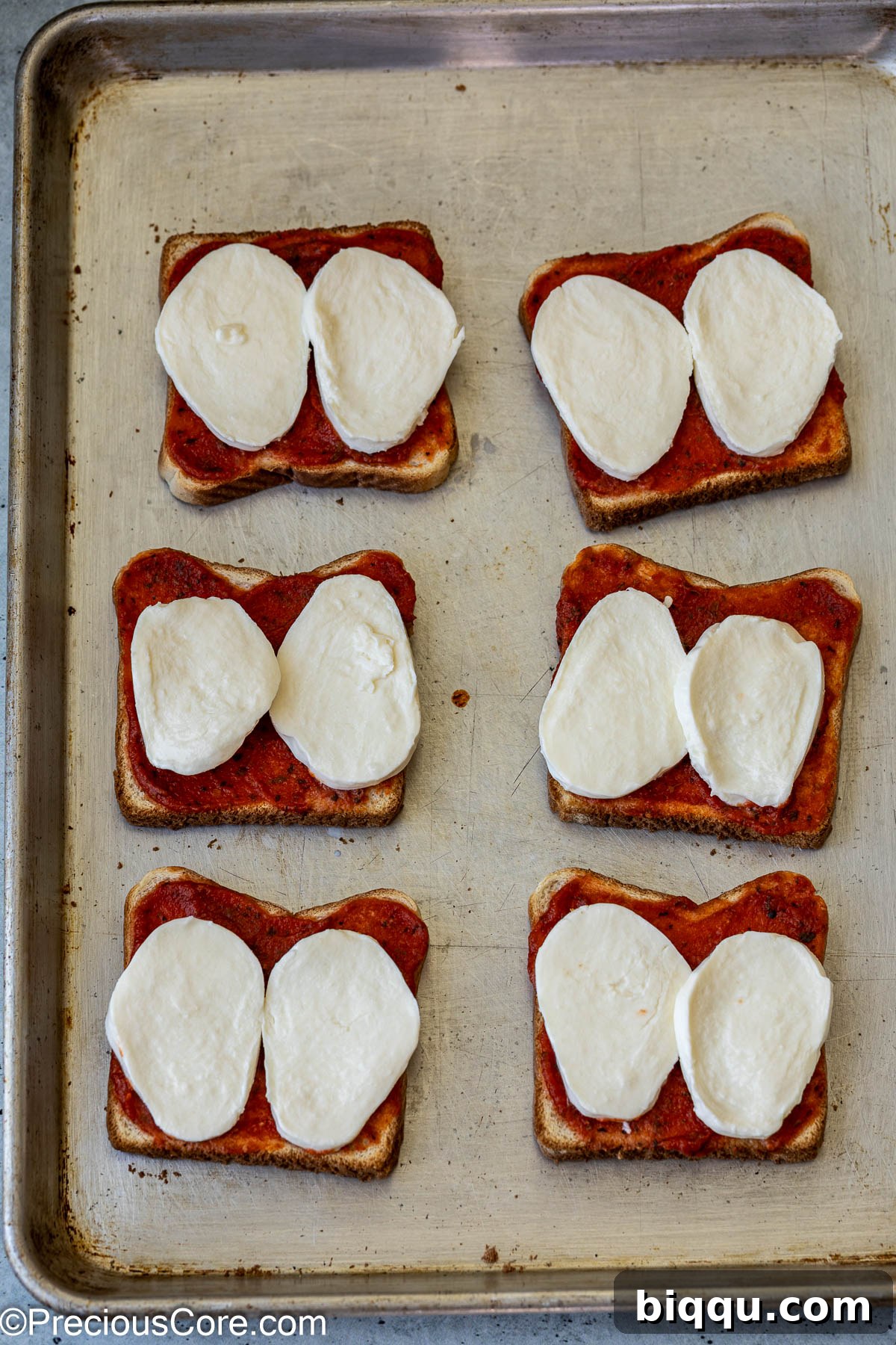 Fresh mozzarella slices carefully placed on top of sauced bread slices.